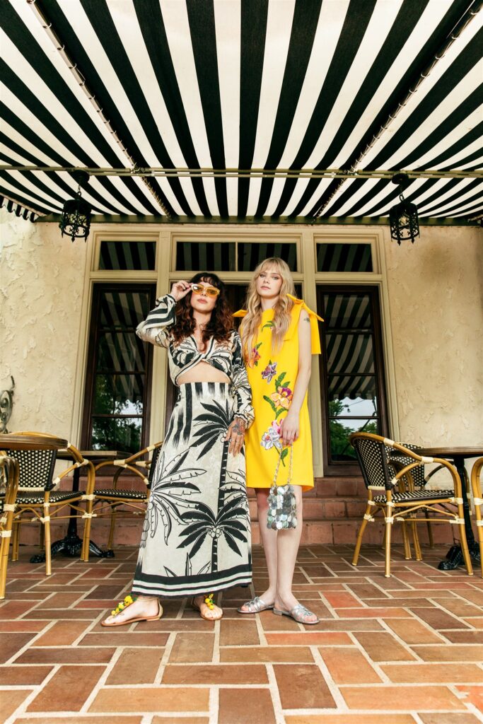 Melanie Packer (left) wears Johanna Ortiz Crop Top ($850) & Skirt ($950); Aquazzura Sandals ($875); and Loewe Cat-Eye Sunglasses ($217)