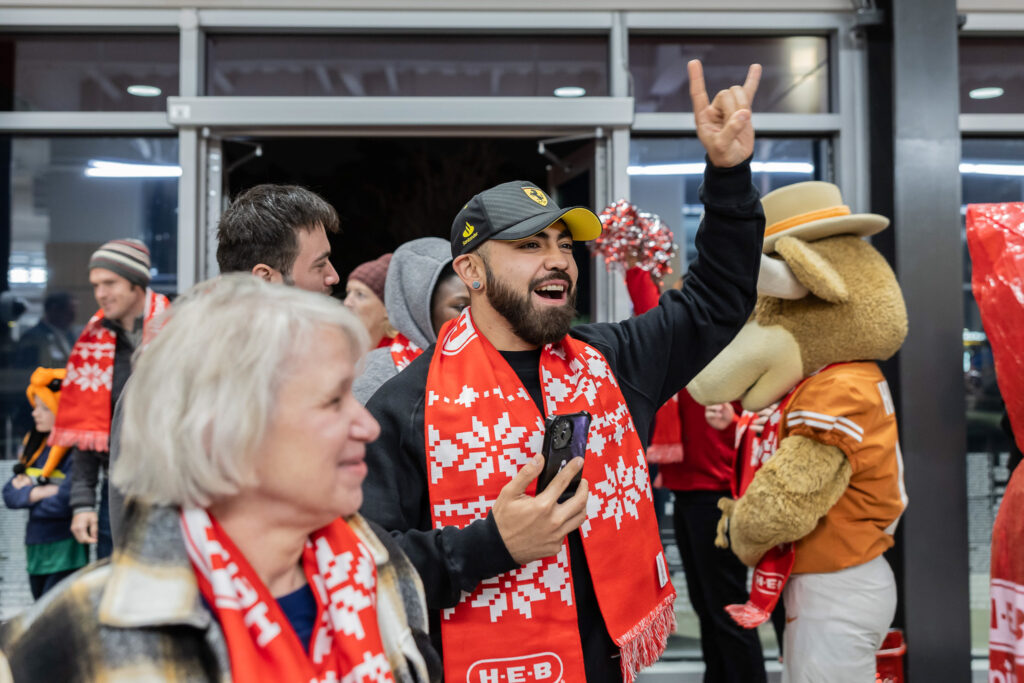 A shopper raises his hand in a "Hook 'em" sign as University of Texas cheerleaders and Bevo, the UT mascot, welcome customers at the H-E-B South Congress grand opening.