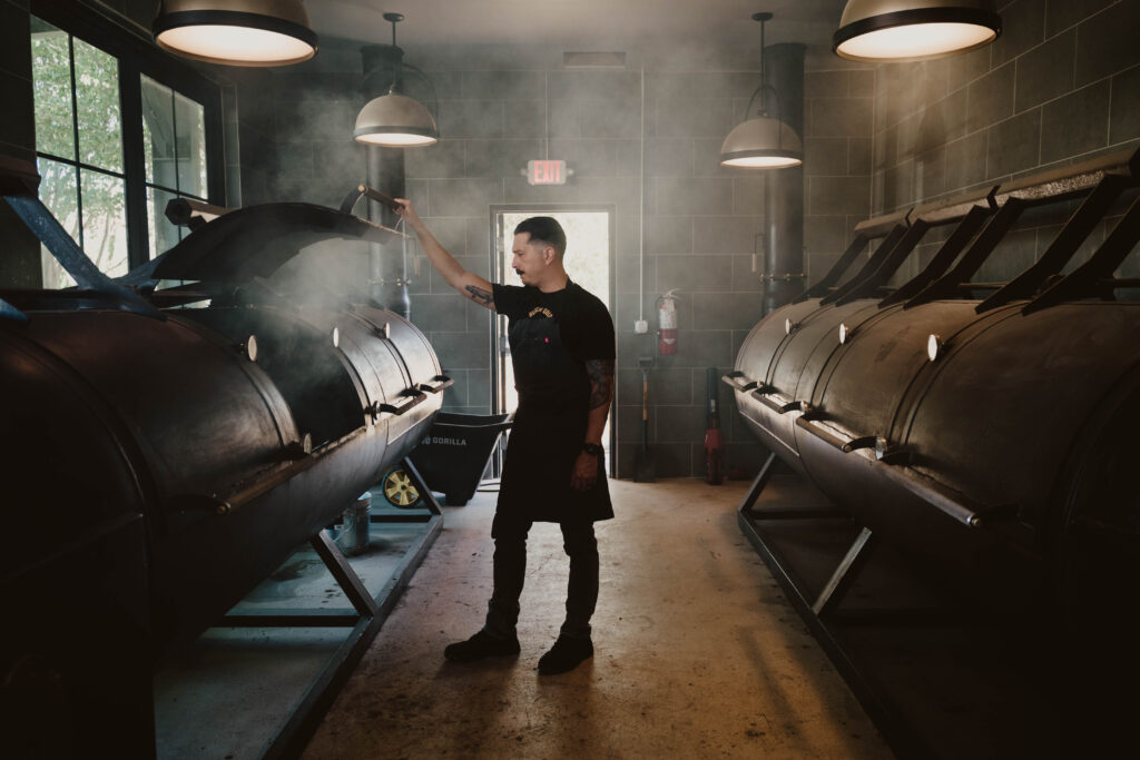 Black Gold owner and pitmaster Mems Davila smokes meats at his custom smokers, named Stevie Ray and Jimmy (Vaughan). (Photo by Randi Reding)