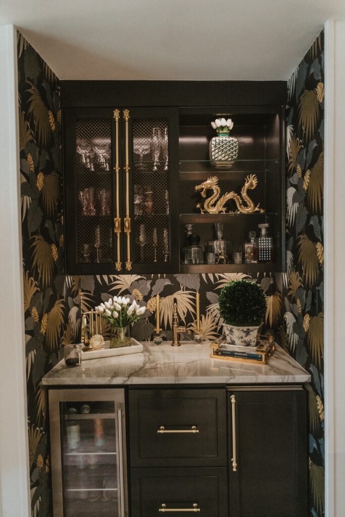 The home bar area features black cabinets with brass accents, palm-patterned wallpaper, and a white marble countertop. (Photo Lemon Woman Photography)