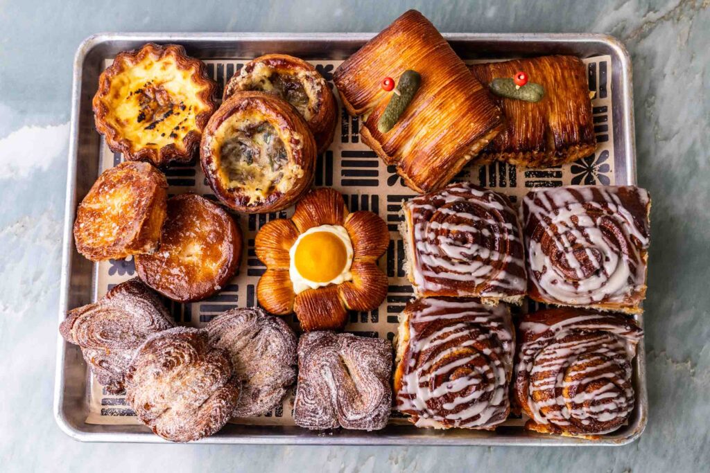 Bottom left morning bun Bottom right cinnamon roll Top right ham and cheese Center poppy Above poppy French onion danish To the left of that is egg tart under that is kouign amman