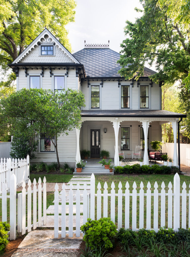 The restored 1890 Queen Anne Victorian at 608 W. Mary St. features a cozy covered front porch with seating, framed by potted plants and lush greenery.