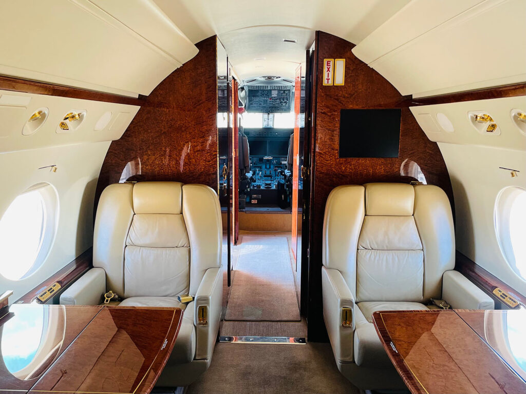 Inside a private jet, view of cockpit and cushioned seating.