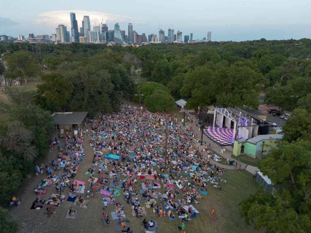 An aerial view shows attendees gathered on the hillside before a summer musical performance at Zilker Hillside Theater in Austin.
