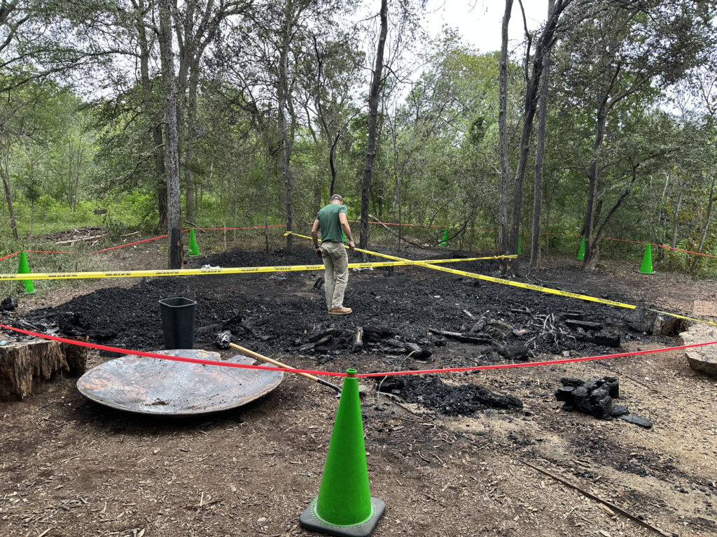 Bret Kiester, director of park operations for Pease Park Conservancy, searches through the ashes of Malin, Thomas Dambo’s troll sculpture, after it burned down Thursday morning at Pease Park