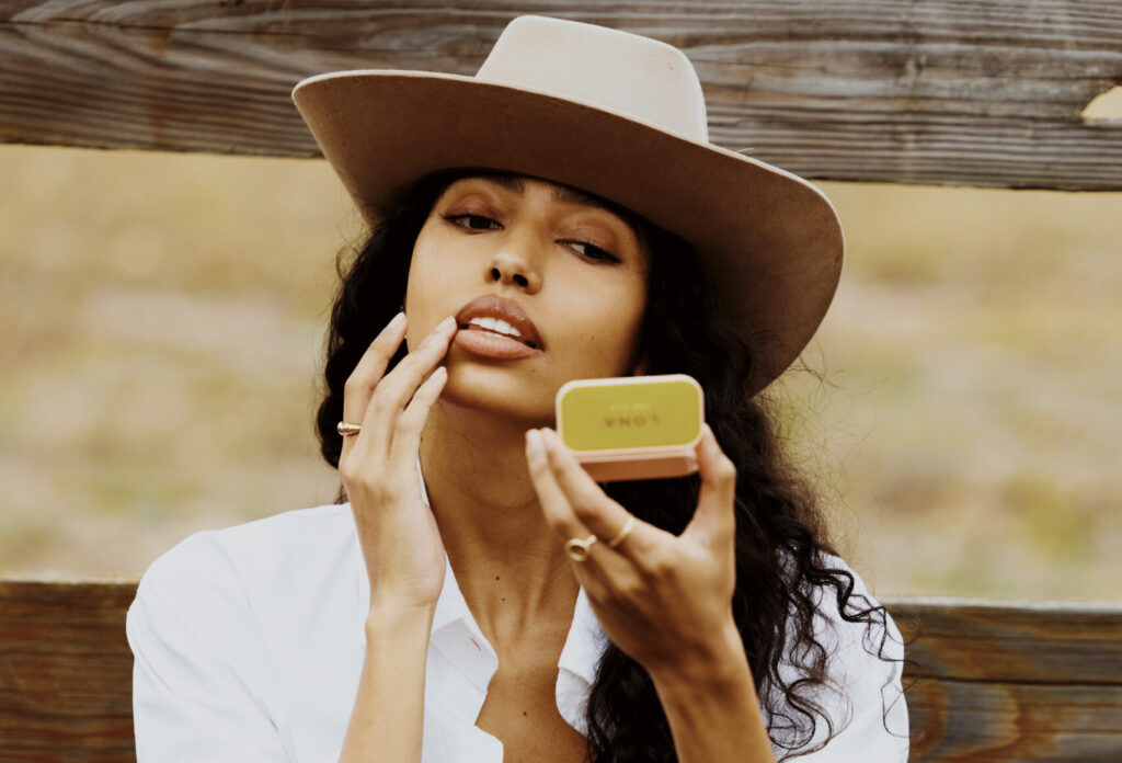 Woman in cowboy hat applies LONA lip balm.