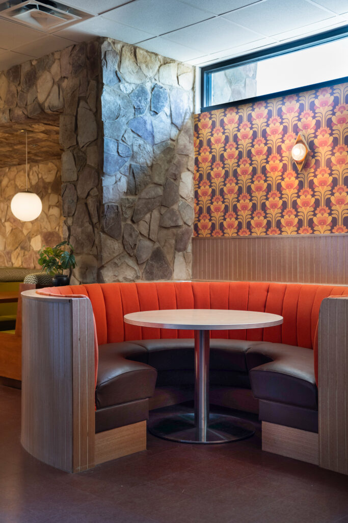 Crescent-shaped booths are paired with retro wallpaper and vintage-style light fixtures at A Little Shady in Kyle.