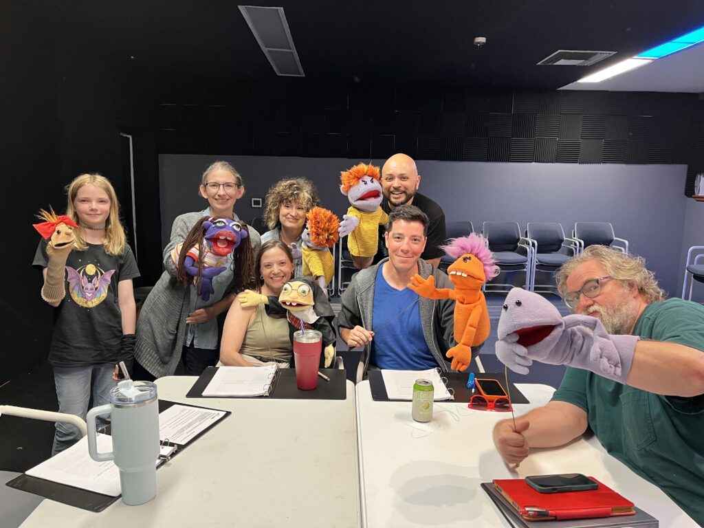 The cast of Kleo James Ryan’s “Lulu Goes to the Jim Henson Memorial Service” gathers around a table with their puppet characters during rehearsal for Austin Playhouse’s 2026 Festival of New Texas Plays.