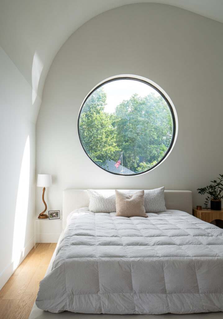 Curved forms carry through a bedroom at Terraluz, where a circular window above the bed echoes the home’s sculptural design.
