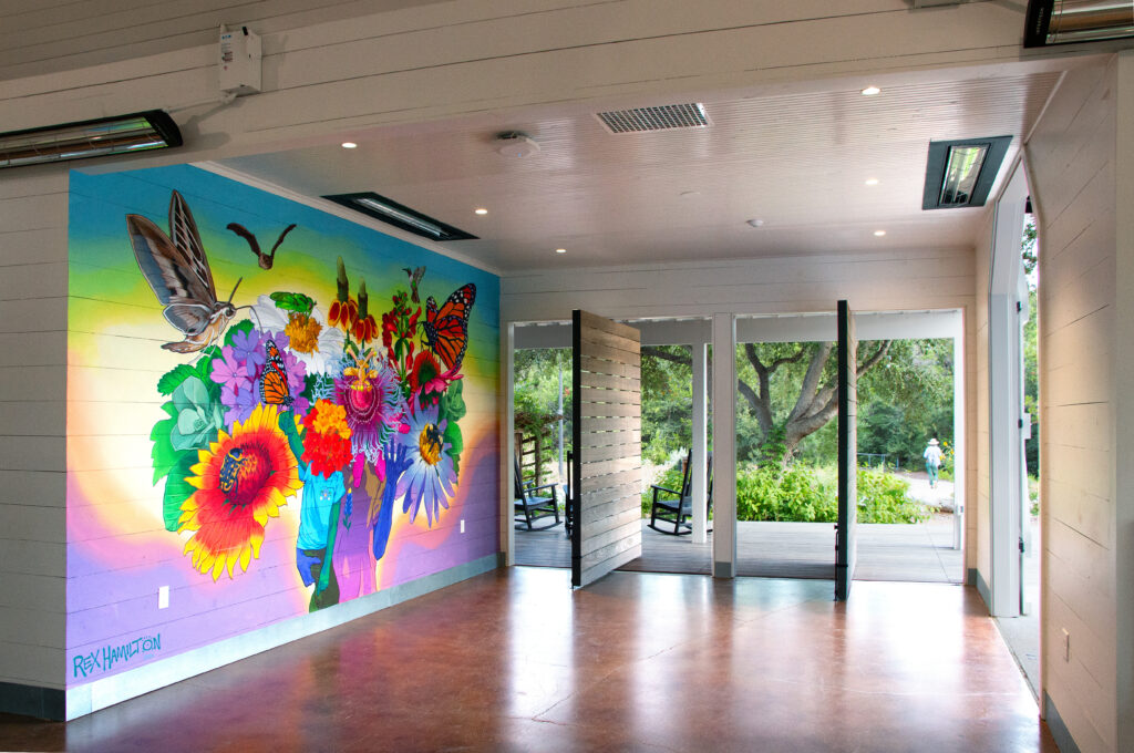 Austin artist Rex Hamilton’s mural depicts native plants and pollinators, offering a preview of the garden planned around the carriage house.